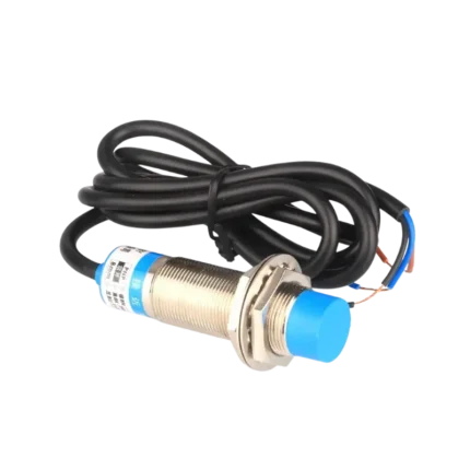 M18 cylindrical inductive proximity sensor showcasing a solid, silver-colored threaded metal casing, a distinct blue plastic sensing head, dual metallic nuts, and a thick black three-conductor output cable.